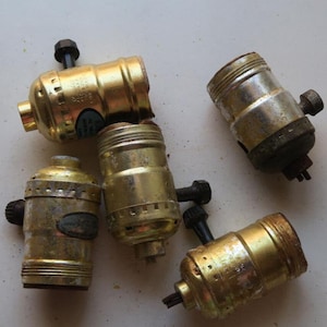 May include: Five brass light bulb sockets with a black screw on the side. The sockets are in various states of wear and tear.
