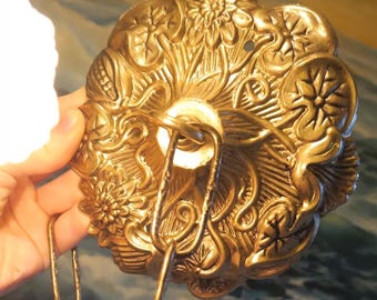 Op de afbeelding: Goudkleurige metalen plafondbevestiging met een decoratief bloemmotief. De bevestiging heeft een haak om een ​​lichtfitting op te hangen.