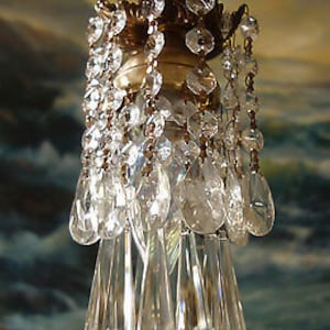 May include: A vintage chandelier with clear crystal teardrop pendants and smaller crystals. The chandelier has a gold-colored metal frame with decorative leaf accents. The crystals are suspended from the frame, creating a sparkling effect.
