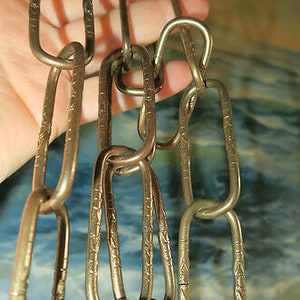 May include: A gold chain with oval links, each link has a decorative pattern. The chain is made of metal and has a shiny finish.