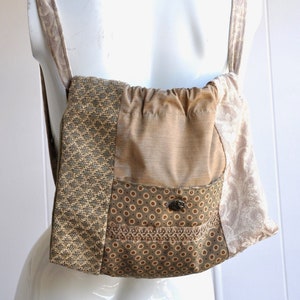 Peut inclure: Un sac à dos en tissu patchwork marron et beige avec une fermeture à cordon et une petite poche sur le devant. Le sac à dos a un motif floral et une fermeture à bouton.