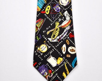 May include: A black silk tie with a colorful pattern of New Orleans themed imagery, including musical instruments, food, and text. The text includes "Bourbon St", "Beignet", "Po-boy", "Big Easy", "French Quarter", "Lake Pontchartrain", "Coffee Jack", "Chartres St", "Zydeco", "New Orleans", and "Chicory".