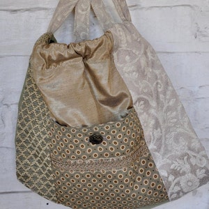 Puede incluir: Una bolsa de mano de lona de color verde, marr&oacute;n y beige con un cord&oacute;n de ajuste en la parte superior y un peque&ntilde;o bolsillo en la parte delantera. La bolsa tiene un cierre de bot&oacute;n y un ribete de encaje.