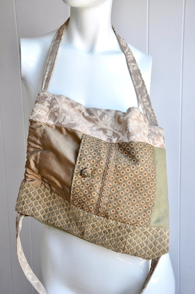 Puede incluir: Un bolso tote de patchwork con una combinaci&oacute;n de colores verde, marr&oacute;n y beige. El bolso tiene una sola correa y est&aacute; hecho de diferentes telas con varios patrones.