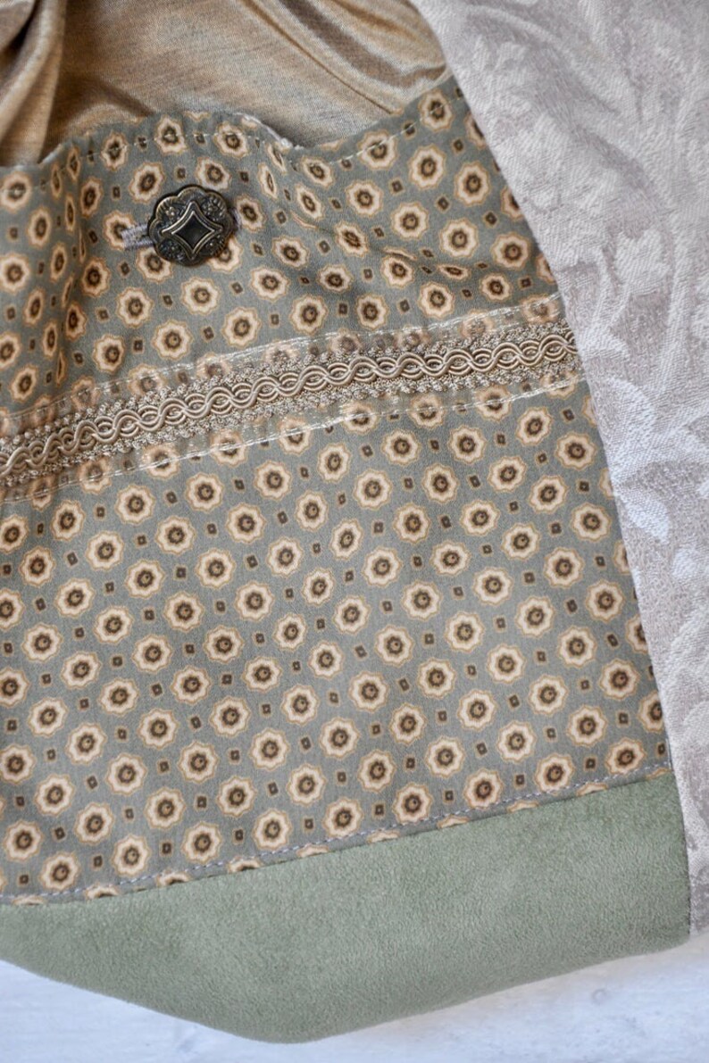 Puede incluir: Primer plano de una tela verde con un patr&oacute;n floral marr&oacute;n y blanco. La tela tiene un ribete marr&oacute;n y una trenza decorativa. Un bot&oacute;n de metal es visible en la esquina superior izquierda.