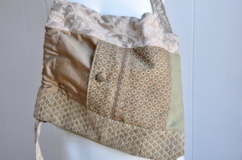 Puede incluir: Un bolso tote de patchwork beige y verde con un patr&oacute;n floral, un bot&oacute;n y un bolsillo peque&ntilde;o. El bolso tiene una correa larga y est&aacute; hecho de diferentes telas.