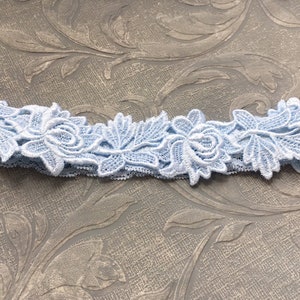 May include: A light blue lace garter featuring floral and leaf designs. The garter is made of delicate lace and has an elastic band. The floral details are intricately designed, adding a touch of elegance. This item is suitable for weddings and special occasions.