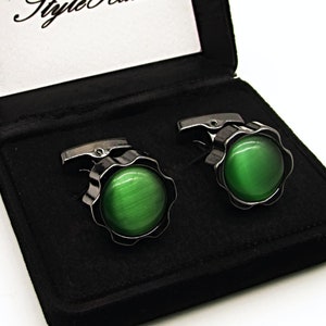 May include: A pair of cufflinks in a black velvet box. The cufflinks are silver with a green stone in the center. The box has the words "Style Haus" printed on the inside.