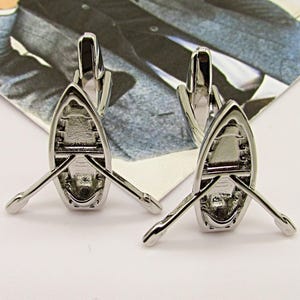 May include: Silver cufflinks with a detailed design of a rowboat with oars.