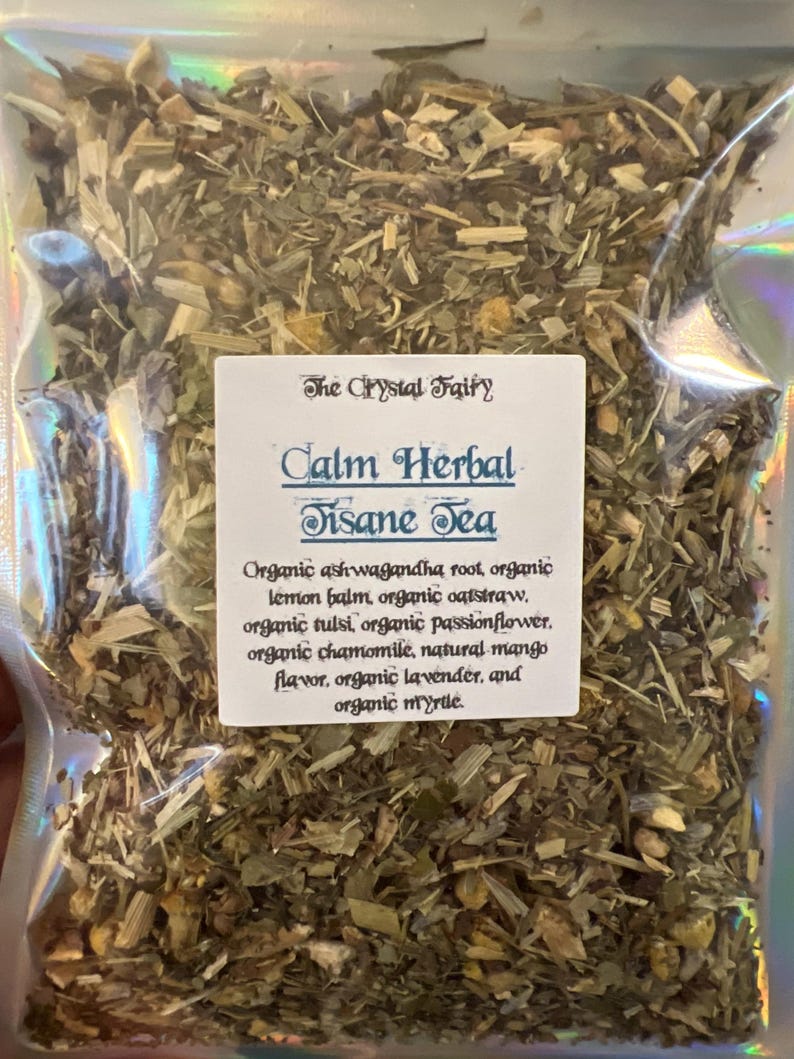 May include: A clear plastic bag filled with dried herbs and labeled "Calm Herbal Tisane Tea" by The Crystal Fairy. The label lists ingredients like organic ashwagandha root, lemon balm, oatstraw, tulsi, passionflower, chamomile, mango flavor, lavender, and myrtle.