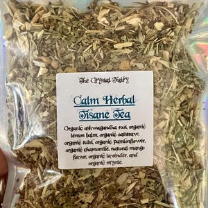 May include: A clear, iridescent bag filled with dried herbs and tea leaves. A white label reads "The Crystal Fairy" and "Calm Herbal Tisane Tea." Ingredients include ashwagandha root, lemon balm, oatstraw, tulsi, passionflower, chamomile, mango flavor, lavender, and myrtle.