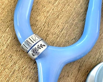 May include: A light blue stethoscope with a silver name tag that reads "CLAIRE" with a small floral design.