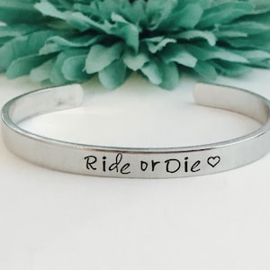 May include: Silver bangle bracelet with the inscription "Ride or Die" and a small heart symbol.