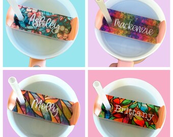 May include: Four clear plastic cups with lids and straws. Each lid has a colorful, patterned sticker with a name on it: Ashley, Mackenzie, Molly, and Brittany.