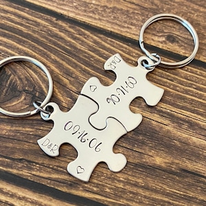 May include: Two silver puzzle piece keychains with a heart and the date "09.16.06" on one piece and "10.11.00" on the other piece. The keychains are engraved with "D&R".
