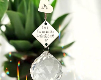 May include: A clear crystal ball suncatcher with a silver-colored metal charm that reads "Look for me in the rainbows" and a heart charm with the name "Mia". The suncatcher hangs in front of a green plant.