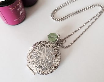 May include: A silver locket necklace with a delicate filigree design. The locket has a small green crystal charm attached to it. The necklace is on a silver chain.