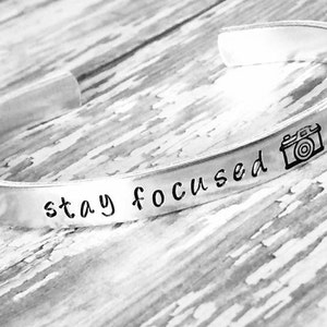 May include: Silver bracelet with the words "stay focused" and a camera icon engraved on it.
