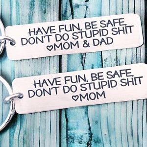 May include: Two silver keychains with the text "HAVE FUN, BE SAFE, DON'T DO STUPID SHIT" and a heart symbol. The top keychain has the text "MOM & DAD" and the bottom keychain has the text "MOM".