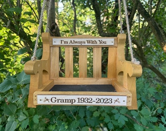 May include: A wooden bird feeder shaped like a swing bench with a black mesh bottom. The feeder has a sign that reads "I'm Always With You" and another sign that reads "Gramp 1932-2023".