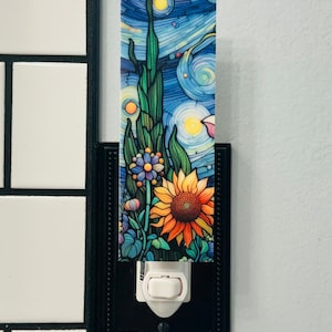 May include: A nightlight with a black frame and a white switch. The front of the nightlight has a colorful image of a sunflower and other flowers against a blue starry sky.