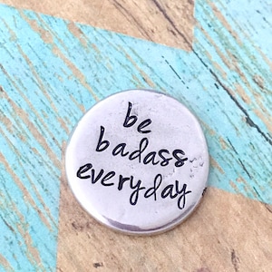 May include: Silver charm with the text "be badass everyday" engraved on it.