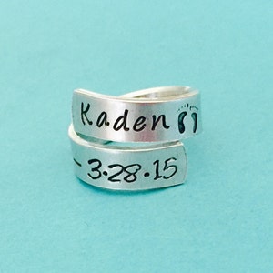 以下が含まれることがあります： 「Kaden」という名前と足跡のシンボルが刻まれた銀の指輪。日付「3-28-15」も指輪に刻まれています。