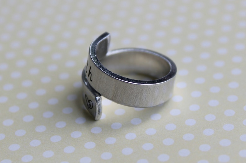 May include: A silver ring with the word "Faith" engraved on the band. The ring is made of metal and has a simple design.