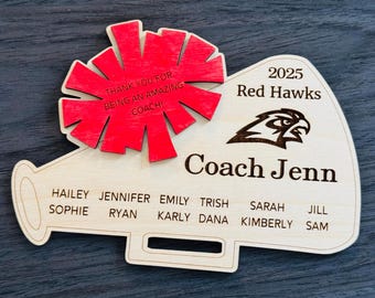 May include: A wooden megaphone with a red pom-pom and the text "Thank you for being an amazing coach!"  The megaphone also has the text "2025 Red Hawks Coach Jenn" and a list of names: Hailey, Jennifer, Emily, Trish, Sophie, Ryan, Karly, Dana, Sarah, Kimberly, Jill, and Sam.