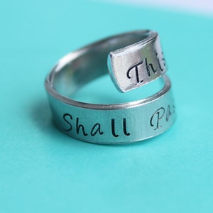 May include: A silver ring with the words "This Shall Pass" engraved on it. The ring is a twist design with the words wrapping around the band.