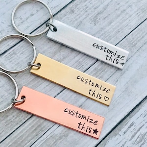 May include: Three silver, gold, and copper keychains with the text "customize this" on each. The silver keychain has a small circle at the end of the text, the gold keychain has a heart at the end of the text, and the copper keychain has a star at the end of the text.