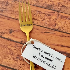 May include: A gold fork with the text "I'm Done." engraved on the handle. A white tag is tied to the fork with the text "Stick a fork in me... I'm done. Retired-2024".