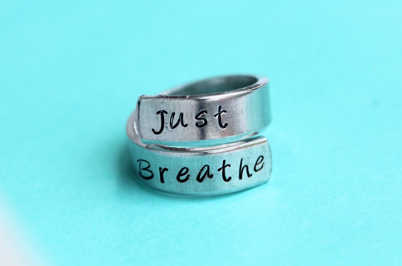 May include: A silver ring with the words "Just Breathe" engraved on it. The ring is open and can be adjusted to fit different finger sizes.