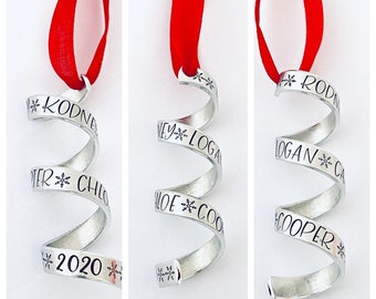 May include: Silver spiral Christmas ornament with a red ribbon. The ornament is engraved with the names Rodney, Ney, Logan, Chloe, Cooper and the year 2020.