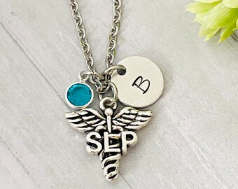 May include: Silver necklace with a blue crystal charm, a silver charm with the letters "SLP" and a silver disc charm with the letter "B".