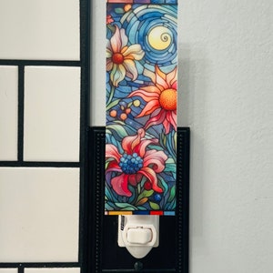 May include: A nightlight with a stained glass design featuring colorful flowers and a crescent moon. The nightlight is plugged into a standard electrical outlet.