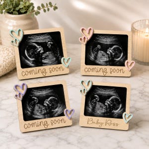 May include: Four rectangular light wood frames, each displaying a black and white ultrasound image. Three frames feature the text 'coming soon' and one features 'Baby Ross'. Each frame is decorated with small, pastel-colored wooden heart cutouts.