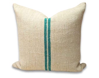 Puede incluir: Cojín cuadrado de tela beige natural con dos rayas verticales turquesas en el centro. La tela texturizada le da un aspecto rústico. Ideal para la decoración del hogar.