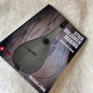 Könnte beinhalten: Ein Buch mit dem Titel "Stick Dulcimer Making: Notes and Plans" von Michael J King. Das Cover zeigt einen grauen Dulcimer mit einem Video-Symbol und den Worten "Video Tutorials".