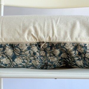 May include: A cream-colored pillow with a zipper closure and a floral patterned fabric. The pillow is sitting on a white chair.