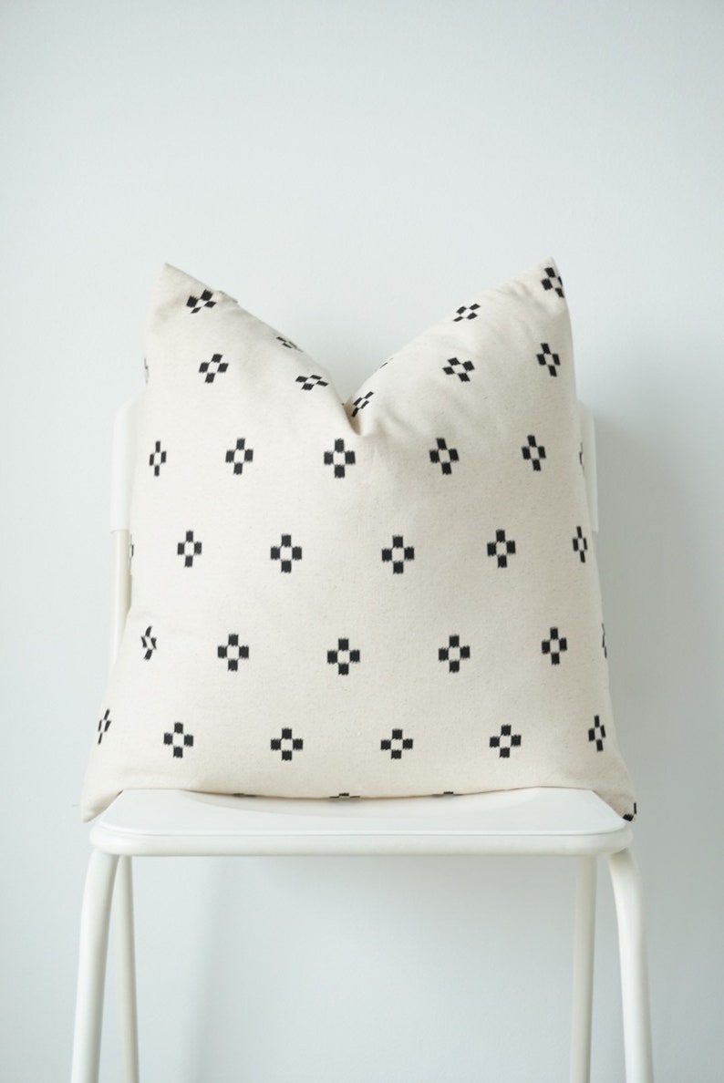 May include: A white pillow with a black geometric pattern. The pillow is sitting on a white chair.
