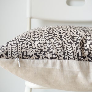 May include: A black and white patterned pillow with a zipper closure. The pillow is sitting on a white chair.