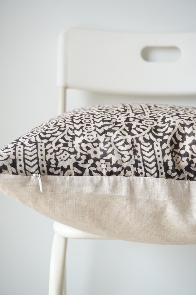 May include: A black and white patterned pillow with a zipper closure. The pillow is sitting on a white chair.