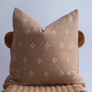 May include: A beige throw pillow with a white geometric pattern. The pillow is sitting on a wooden chair with a woven seat.