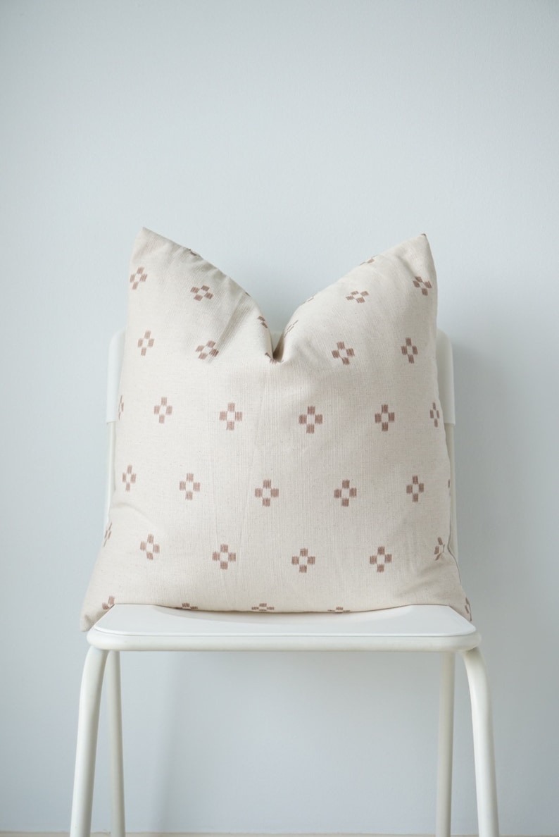 May include: A white chair with a brown and white patterned pillow on the seat. The chair is against a white wall.