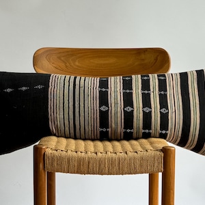 May include: A black and white striped throw pillow with a woven pattern. The pillow is sitting on a wooden chair with a woven seat.