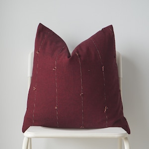May include: A burgundy throw pillow with decorative stitching on a white chair.