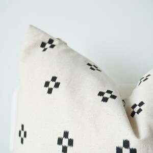 May include: A white pillow with a black and white geometric pattern. The pattern is a series of small squares arranged in a cross shape.
