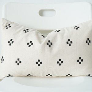 May include: A white pillow with a black geometric pattern. The pillow is sitting on a white chair.