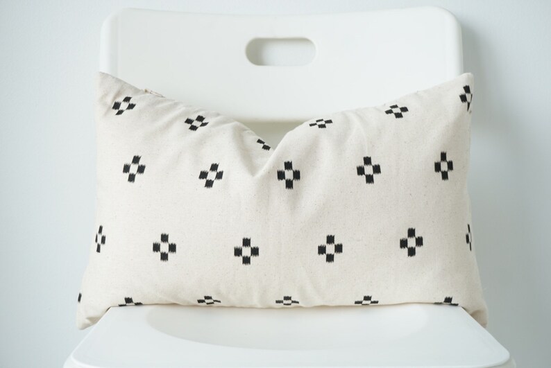 May include: A white pillow with a black geometric pattern. The pillow is sitting on a white chair.